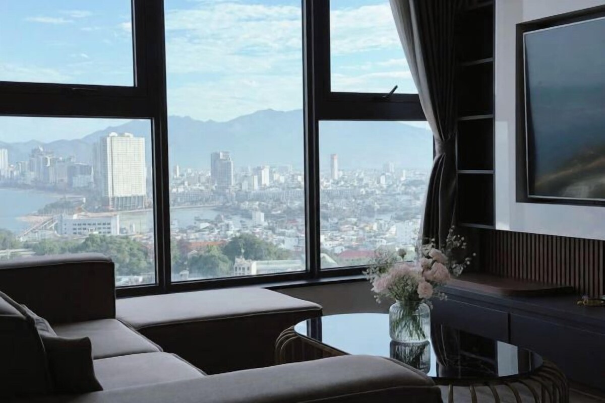 A room with a large window, a sofa, a TV, and a vase with flowers.