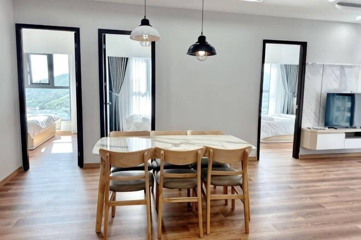 Une chambre d’hôtel moderne avec une table à manger en bois, des chaises, un téléviseur et un balcon avec vue.