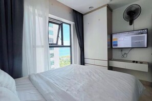 A hotel room with a bed, a window with curtains, a wall-mounted TV, and a ceiling fan. - NATA (Nha Trang)