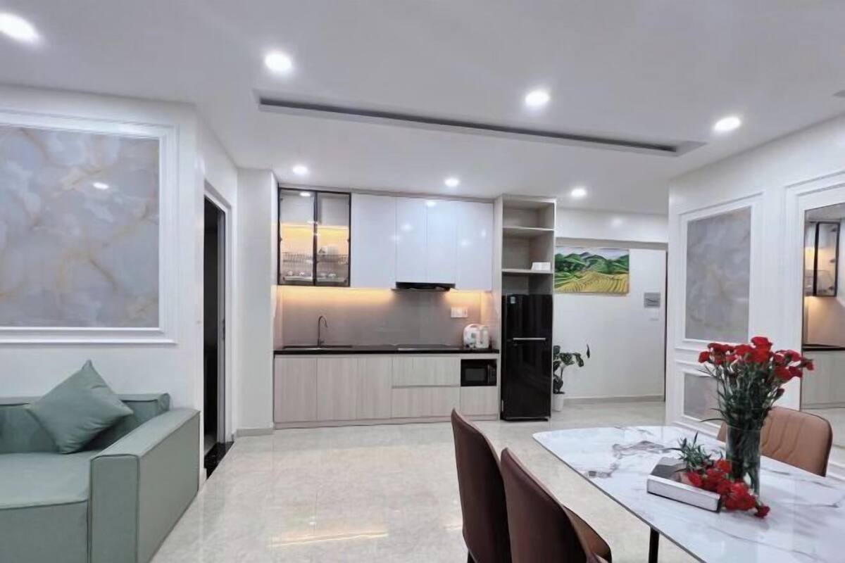 Une cuisine moderne avec des meubles blancs, un réfrigérateur noir et un coin repas comprenant une table et des chaises en marbre.