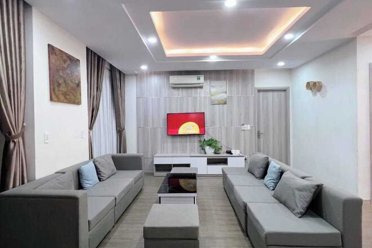 Un salon moderne comprenant un ensemble de canapés, une table basse, un téléviseur à écran plat et un climatiseur fixé au mur.