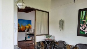 Una habitación con pared de piedra, una pequeña mesa con planta en maceta, dos sillas, un cuadro de flores y una planta colgante.