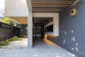 Une entrée moderne avec un passage couvert, une clôture noire et un mur agrémenté d’un luminaire circulaire.
