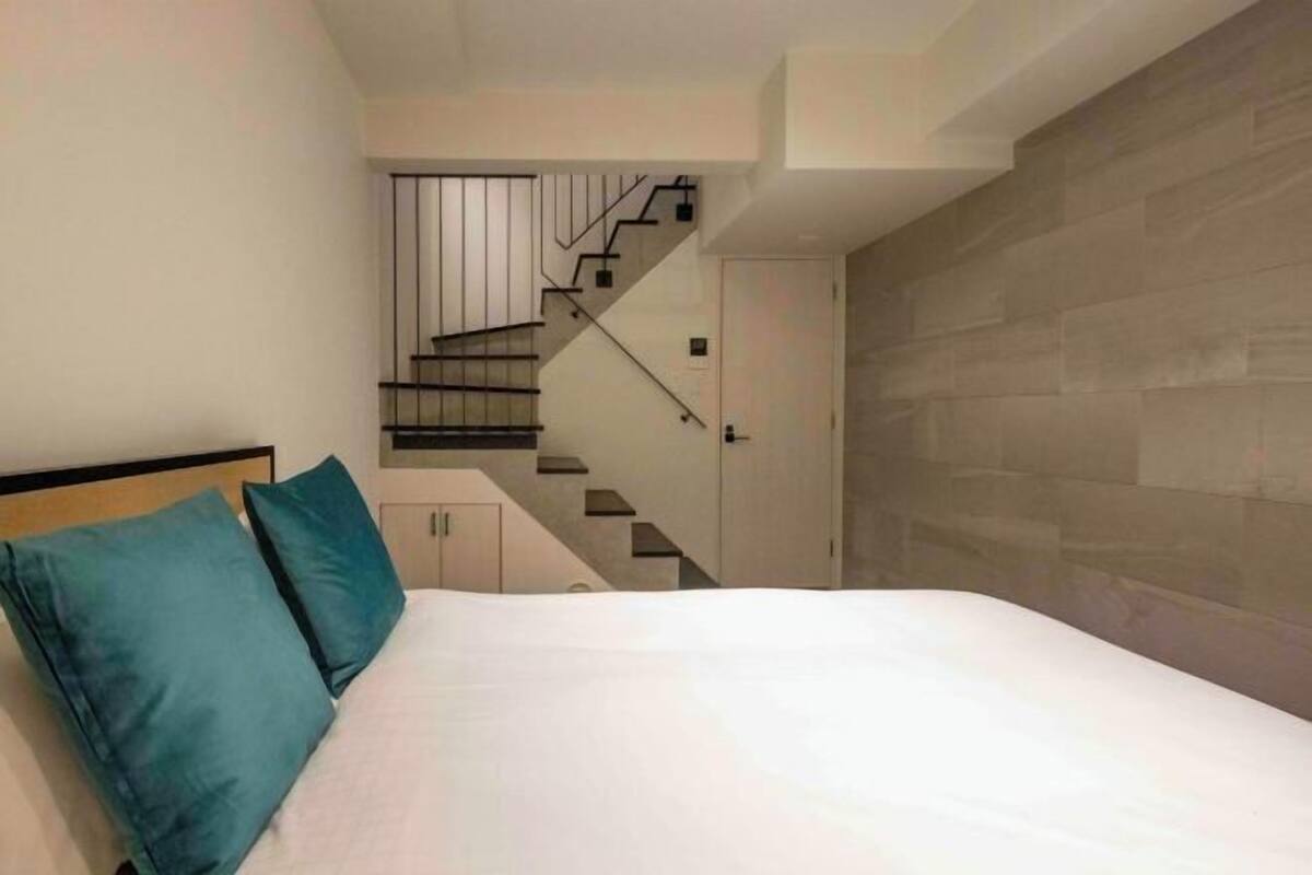 A bedroom with a bed, teal pillows, a staircase, and a wooden wall.
