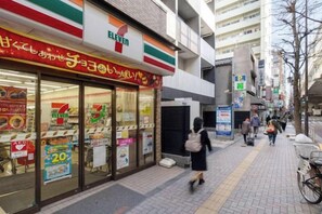 A 7-Eleven convenience store with a clear glass front, located on a city street with pedestrians and a bicycle. - LEGALAND Hatagaya (Tokyo)