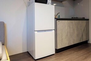 A compact kitchen with a white refrigerator, a wooden cabinet, and a countertop. - LEGALAND Hatagaya (Tokyo)