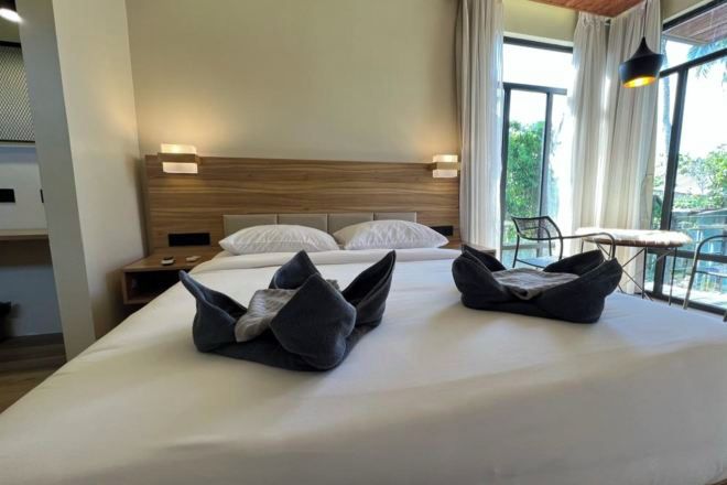 Hotellihuone, jossa on sänky, yöpöydät, pöytä ja näkymä vihreälle alueelle.