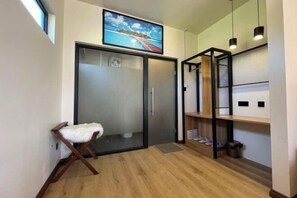Casa de banho moderna com cabine de duche em vidro, um banco de madeira e um armário com sapatos.