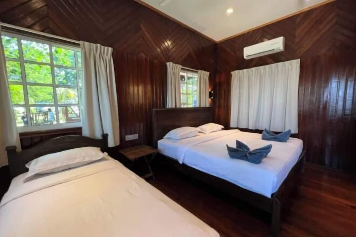 A bedroom with two beds, wooden walls, a window with curtains, and an air conditioning unit.