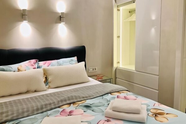 A neatly made bed with floral bedding, a bedside table, and a wardrobe with a mirror.