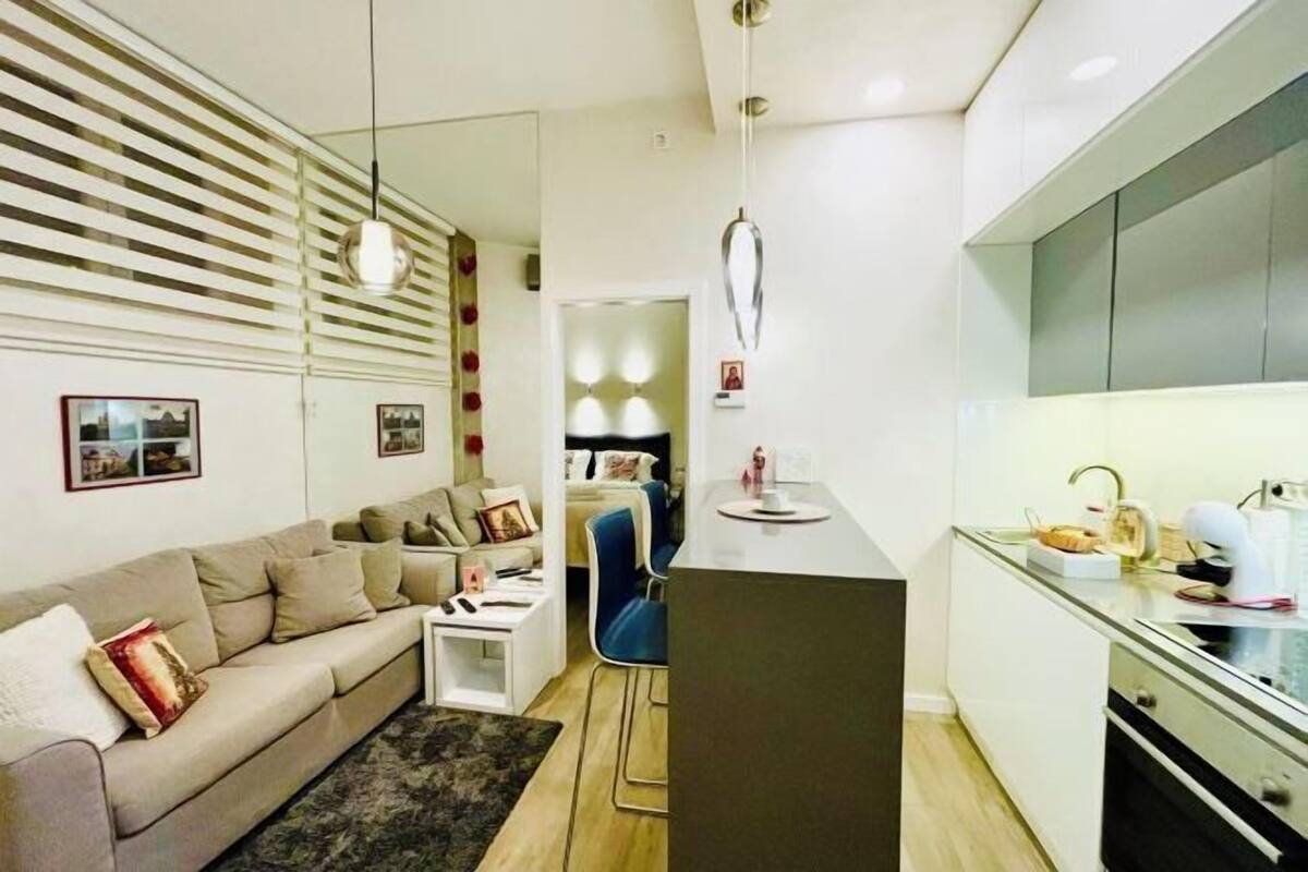 A modern living room with a sofa, a coffee table, and a dining area with a kitchen counter.