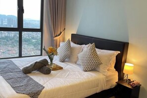 A neatly made bed with patterned pillows, a bedside lamp, and a view of a cityscape through a large window. - 7 Pax Genting View Nearby Mont Kiara Desa Park 500Mbps Netflix (Kuala Lumpur)