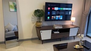 A modern living room with a flat-screen TV mounted on the wall, a dark wooden console table with a lamp, and a plant. - 7 Pax Genting View Nearby Mont Kiara Desa Park 500Mbps Netflix (Kuala Lumpur)