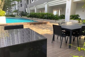 An outdoor pool area with a table and chairs, surrounded by greenery and modern architecture. - 7 Pax Genting View Nearby Mont Kiara Desa Park 500Mbps Netflix (Kuala Lumpur)