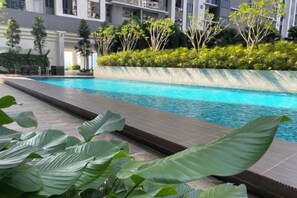 A swimming pool with a tiled edge, surrounded by greenery and a building in the background. - 7 Pax Genting View Nearby Mont Kiara Desa Park 500Mbps Netflix (Kuala Lumpur)