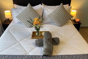 A neatly made bed with patterned pillows, a vase of flowers, and rolled towels on a tray. - 7 Pax Genting View Nearby Mont Kiara Desa Park 500Mbps Netflix (Kuala Lumpur)
