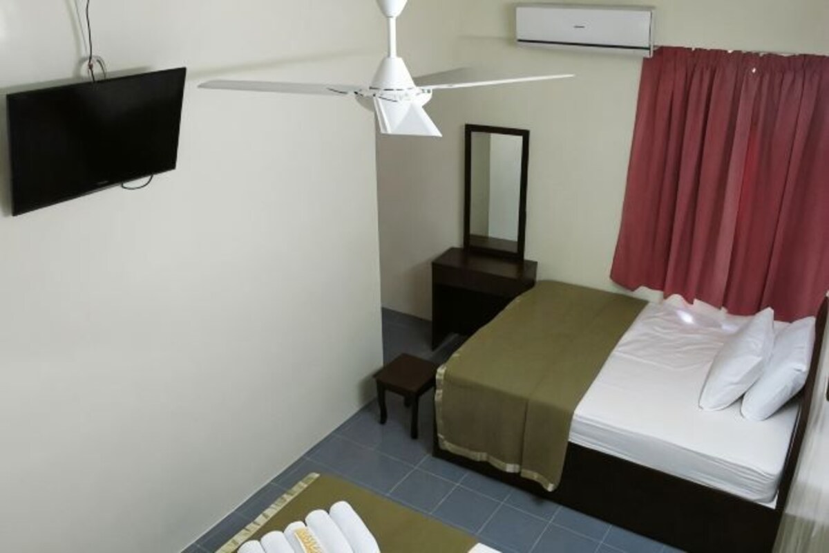 A bedroom with a bed, a ceiling fan, a TV, a mirror, and a red curtain.