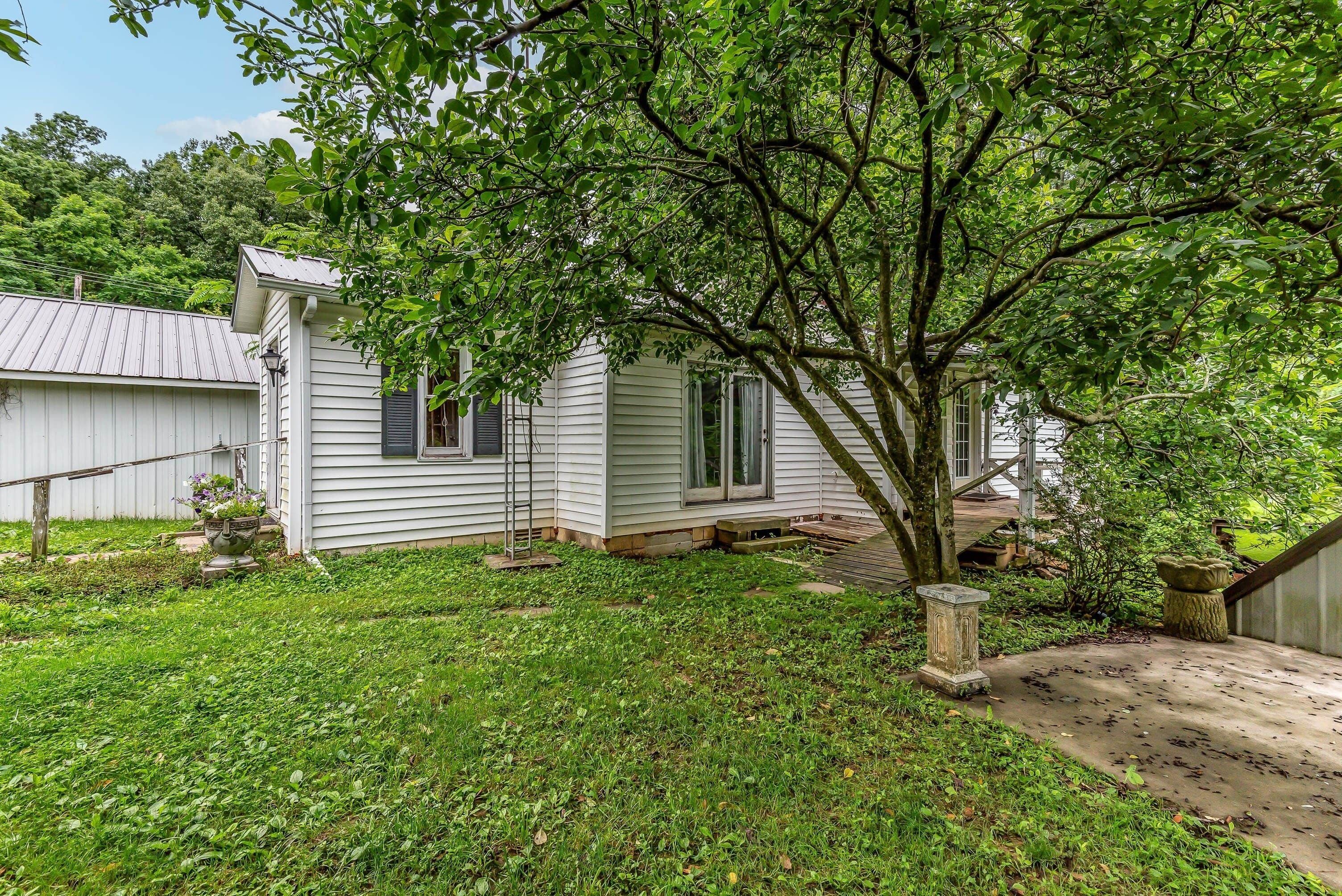 A white single-story house with a front porch, a tree in front, and a small garden area.