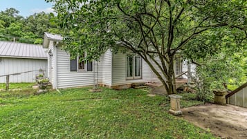 A white single-story house with a front porch, a tree in front, and a small garden area.