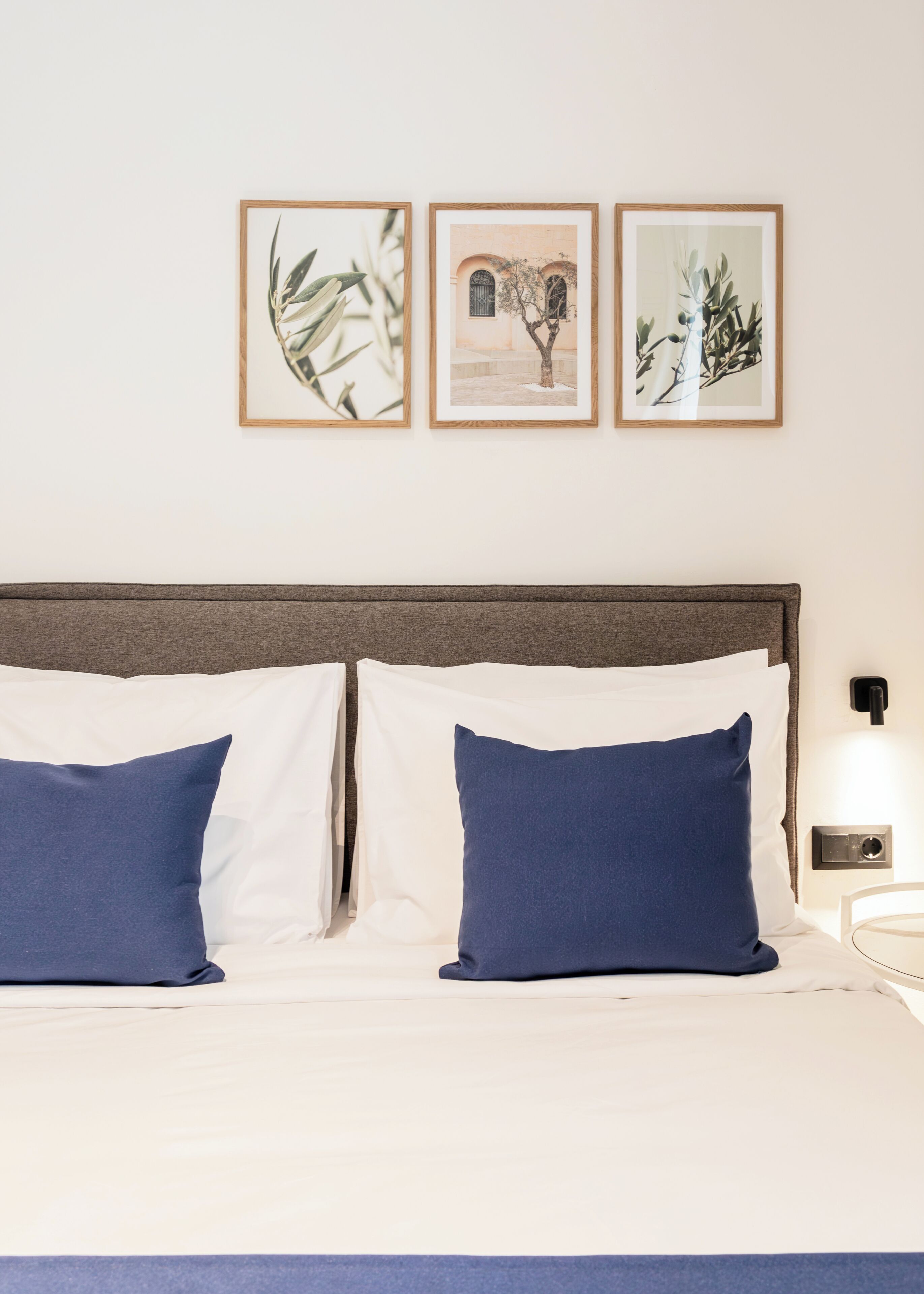 A neatly made bed with white and blue pillows, a wooden headboard, and three framed pictures on the wall above.