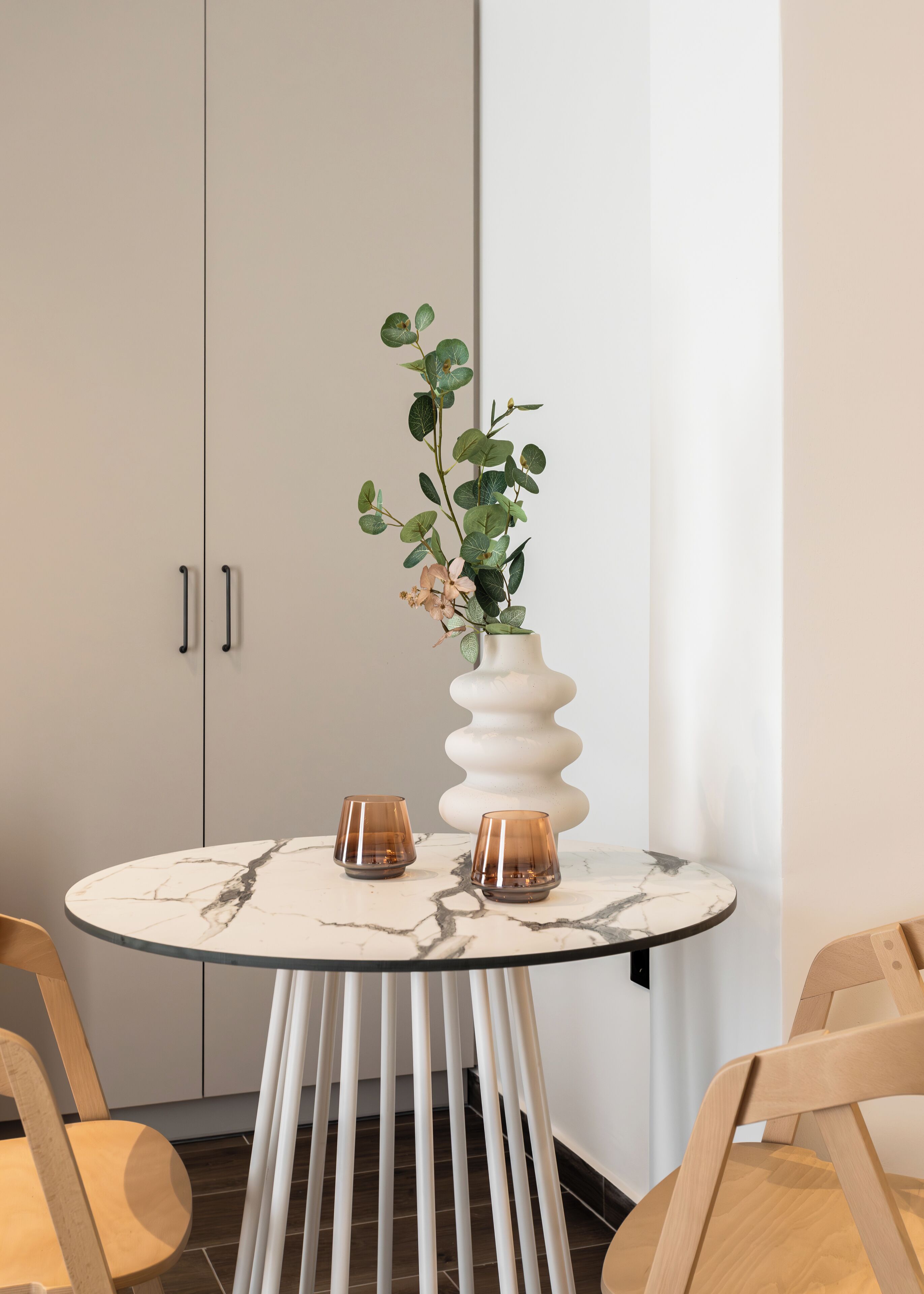 A round table with a marble top, two candle holders, and a tall white vase with a plant.