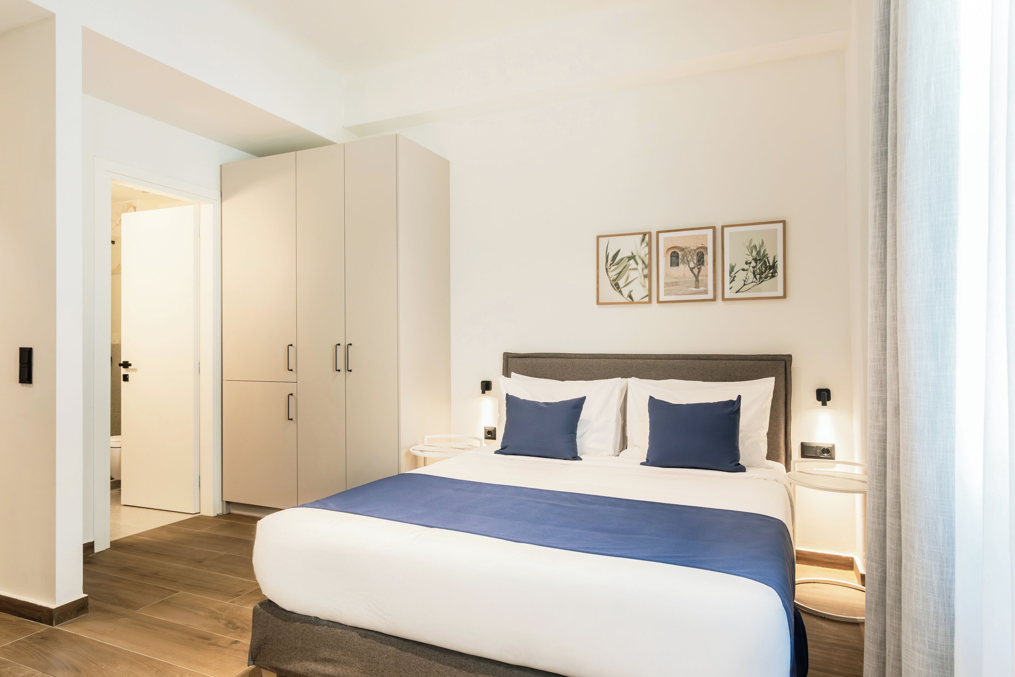 Ein Hotelzimmer mit einem großen Bett, einem Kleiderschrank, einem Nachttisch mit Lampe und gerahmten Bildern an der Wand.