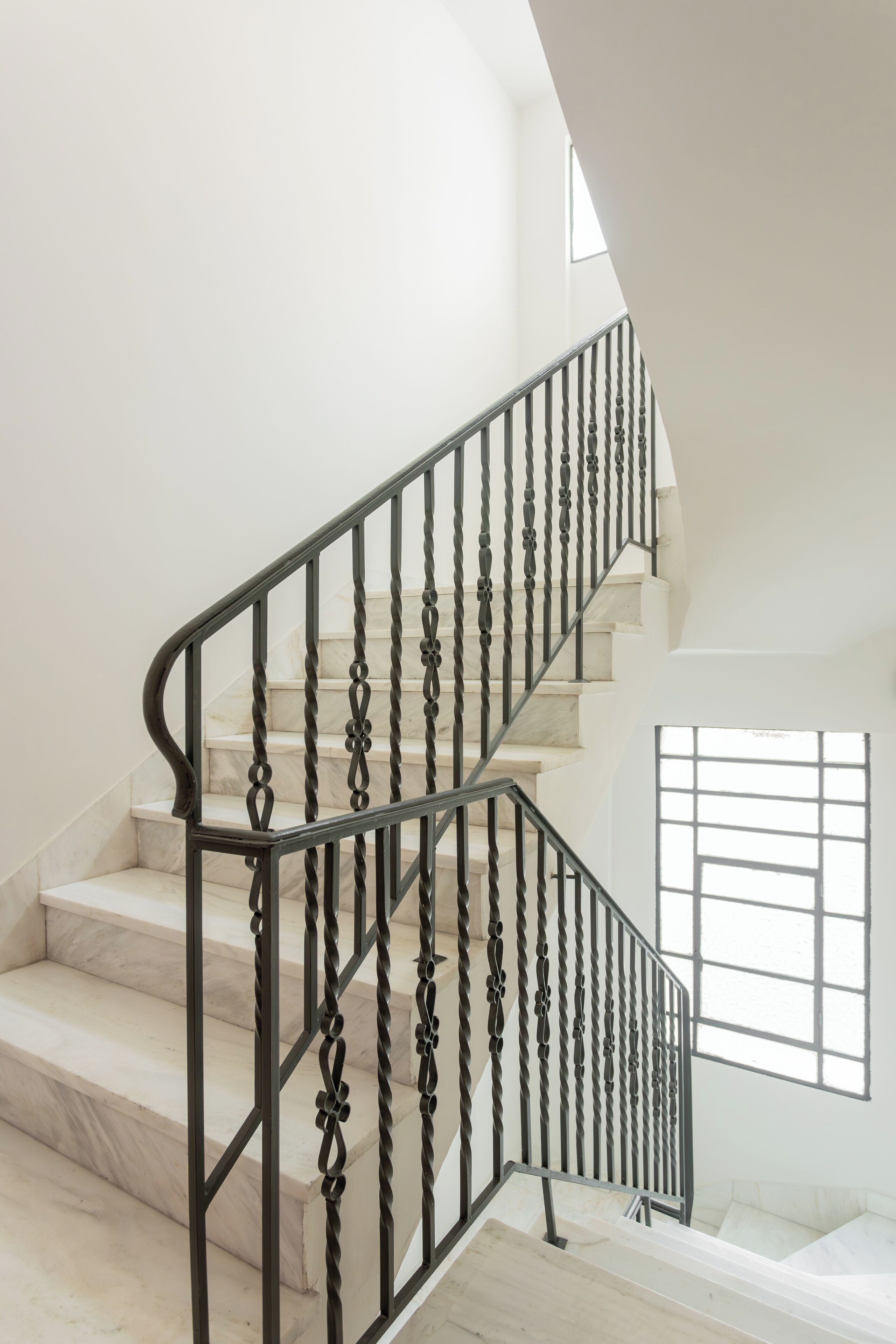 A staircase with a black metal railing, marble steps, and a window with a grid pattern.
