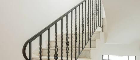 A staircase with a black metal railing, marble steps, and a window with a grid pattern.