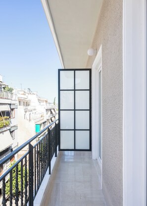 Ein Balkon mit einer schwarzen Glastür, einem Metallgeländer und Blick auf angrenzende Gebäude.