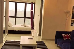 A living room with a sofa, a small table, and a bed with a view. - Layover Living at KLIA South (Sepang)