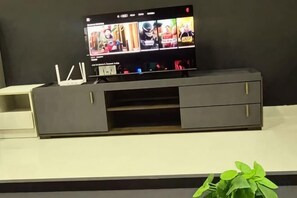 A flat-screen TV on a dark-colored entertainment unit with a plant in the foreground. - Layover Living at KLIA South (Sepang)