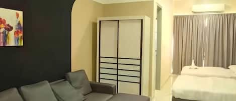 A modern hotel room with a sofa, a small table, a bed, and a wardrobe.