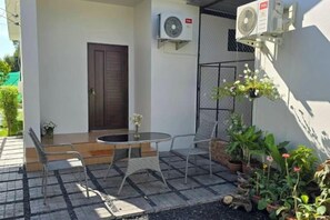 Een terras met een tafel, stoelen, een deur en bloempotten.