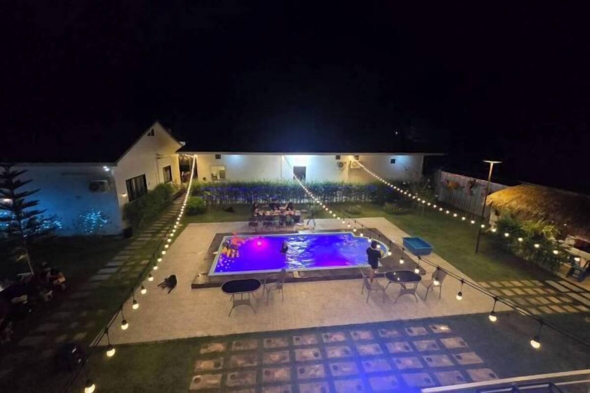 Une piscine entourée de chaises et de tables, le tout illuminé par des guirlandes lumineuses.