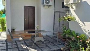 Un espace patio avec une table ronde et deux chaises, une porte et un appareil de climatisation fixé au mur.