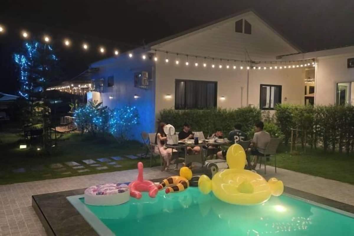 Une piscine avec des jeux gonflables, un espace patio avec des tables et des chaises, et des guirlandes lumineuses.