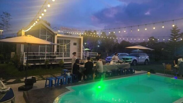 Un espace extérieur aménagé pour les repas, avec des guirlandes lumineuses, une piscine et des parasols.