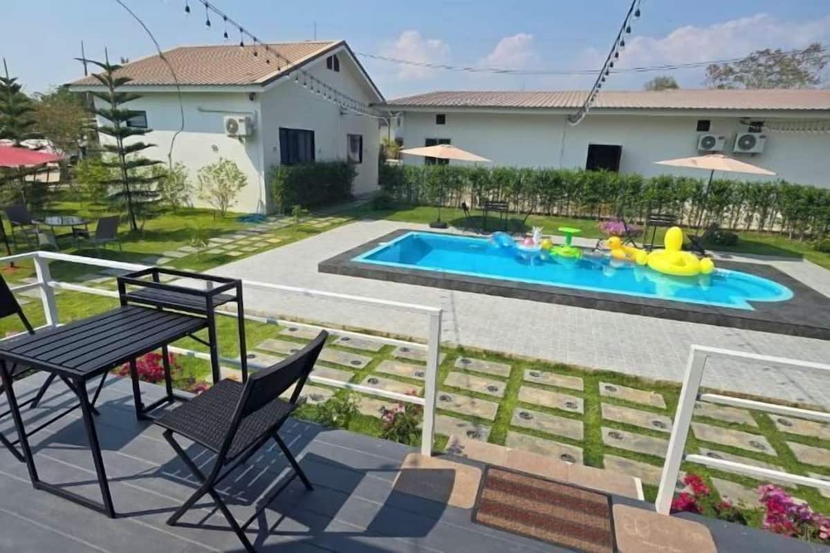 Une piscine avec des jeux gonflables, une terrasse avec des chaises et une table, et une maison avec un toit en tuiles.