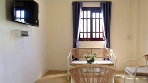 Une pièce dotée d’un téléviseur à écran plat fixé au mur, d’une fenêtre avec des rideaux, d’une table avec des chaises et d’un petit vase avec des fleurs.
