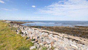 A coastal landscape with a rocky shoreline, grassy areas, and a clear sky.