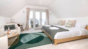 A bedroom with a bed, a round coffee table, a chair, a window with curtains, and a view of the outside.