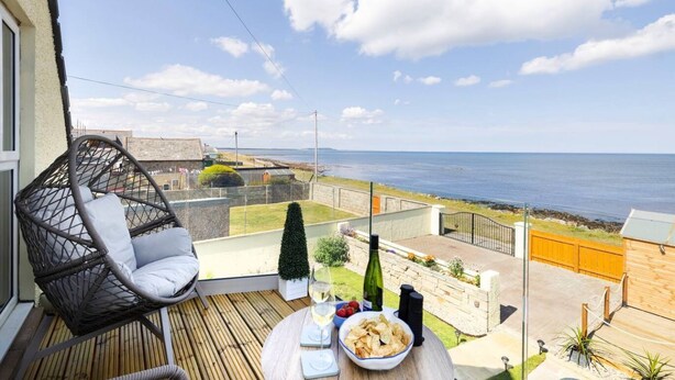 A balcony with a wicker chair, a table with snacks and a bottle, and a view of the sea.