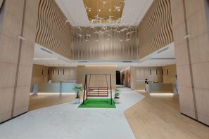 A spacious lobby with a reception desk, a green carpeted area, and a modern ceiling design. - K Avenue by Butter House @Sunset Seaview Cozy (Donggongon)