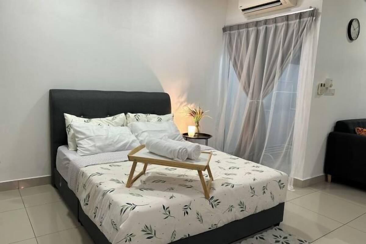 A neatly made bed with a white floral bedspread, a small bedside table with a lamp, and a window with sheer curtains.