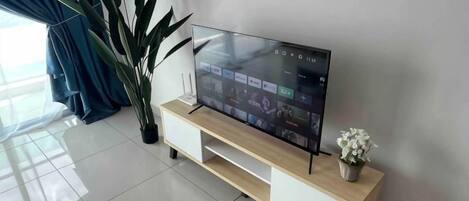 A flat-screen TV on a wooden TV stand with a potted plant beside it.