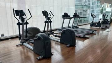 A gym with cardio machines, including treadmills and elliptical trainers, on a wooden floor with large windows.