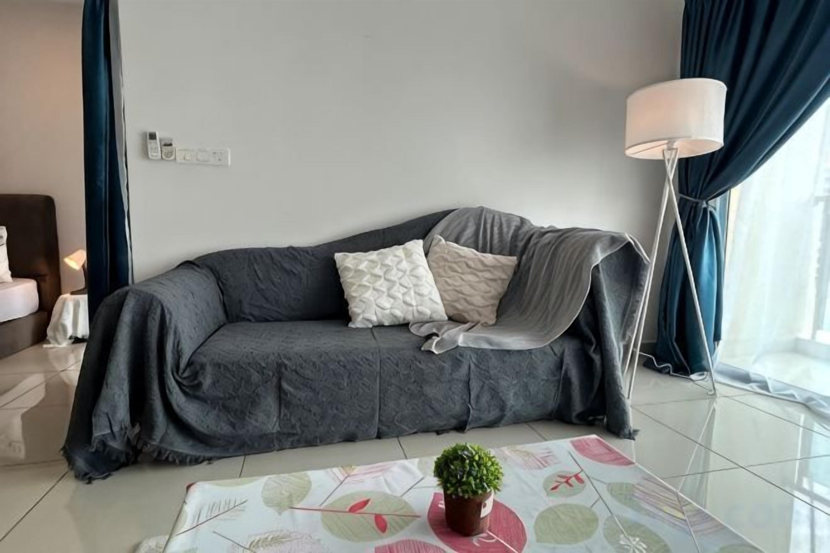 A modern living room with a grey sofa, a small table with a potted plant, and a floor lamp.