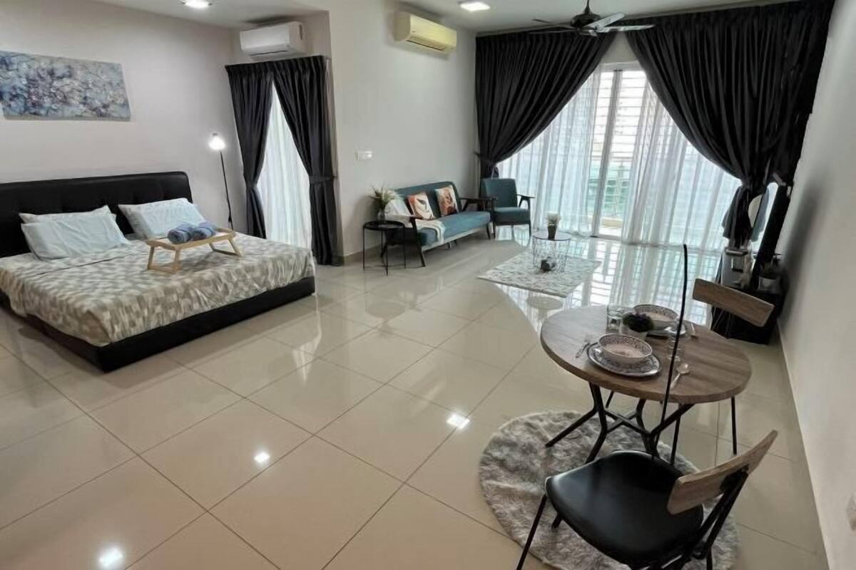A modern living room with a bed, a sofa, a dining table with chairs, and large windows with curtains.