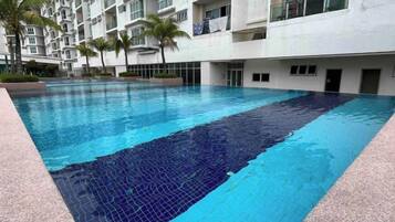 A swimming pool with a tiled edge, surrounded by a multi-story building with balconies.