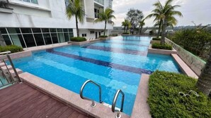 A swimming pool with clear blue water, surrounded by greenery and modern buildings. - M9 Prime Suite@H20 Medalla CittaMall SubangAirport (Petaling Jaya)